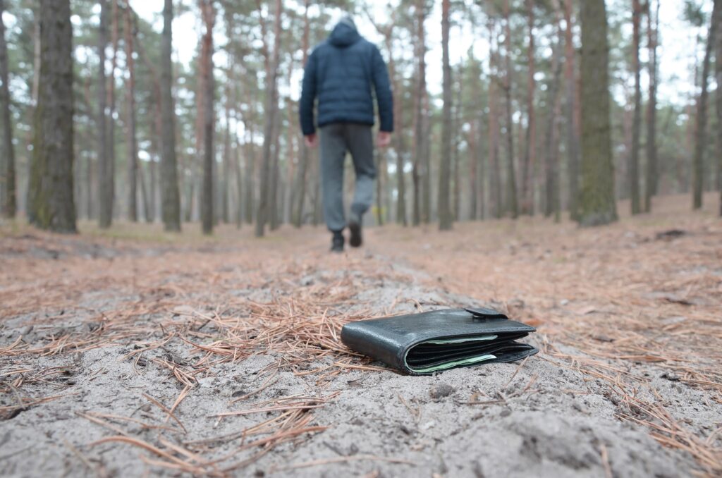 Young man loses his purse with euro money bills on Russian autumn fir wood path. Carelessness and losing wallet concept