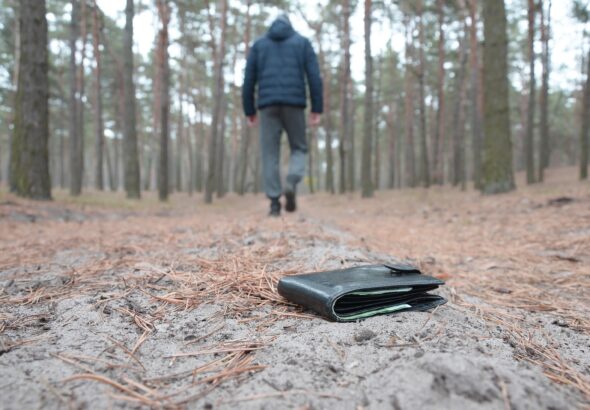 Young man loses his purse with euro money bills on Russian autumn fir wood path. Carelessness and losing wallet concept