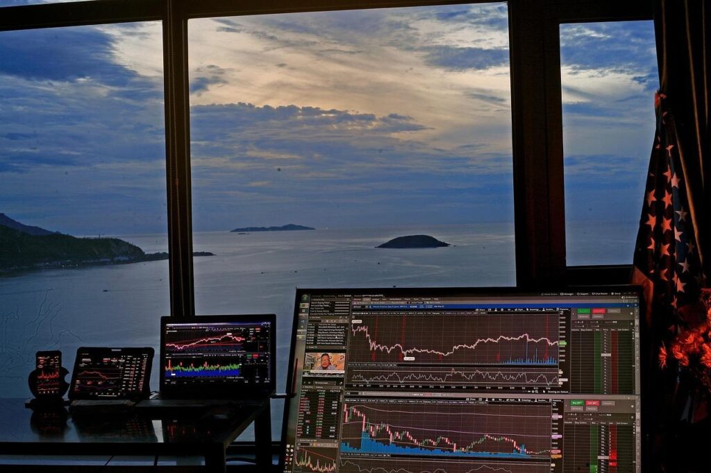 Multiple trading screens with sunset and ocean background