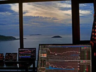 Multiple trading screens with sunset and ocean background