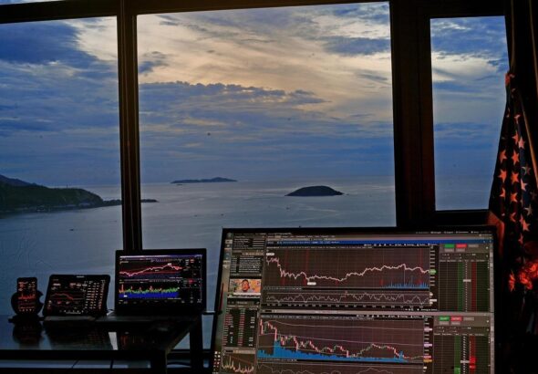 Multiple trading screens with sunset and ocean background